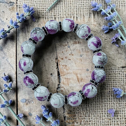 Cherry Pit Crafts stretch bracelet with white glass beads, purple ink details, black accents, and rhinestones. Flexible design.